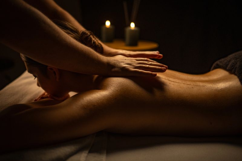 A young woman receives a soothing massage in a dimly lit, serene spa. Gentle hands massage her back, promoting relaxation and wellness. Candles create a calming ambiance, emphasizing the therapeutic and self-care experience.