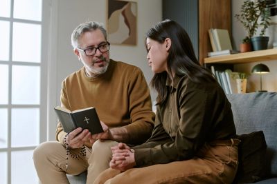 Man holding a Bible, talking with woman on couch.