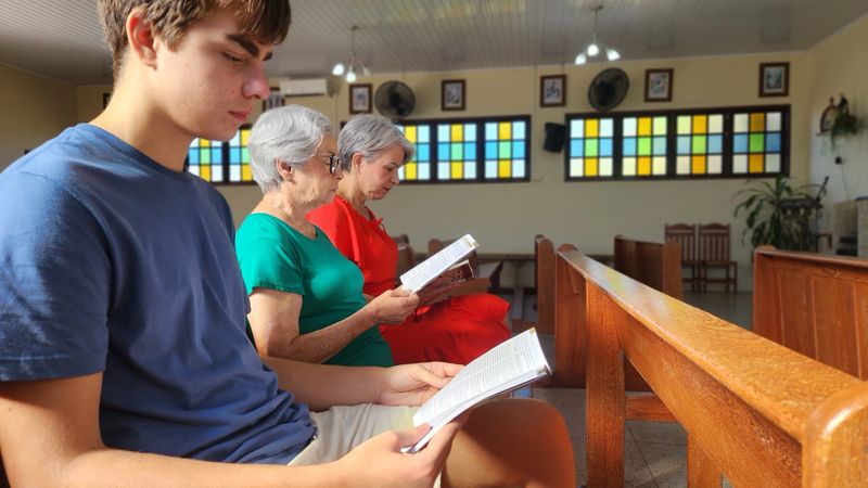 Grandmother, mother, and son sitting, reading together in the Catholic church.