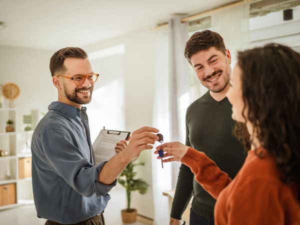 Real estate agent handing over keys to happy new homeowners in bright living room.