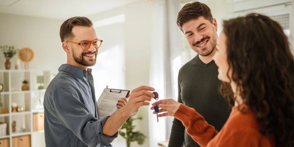 Real estate agent handing keys to a happy couple in a bright room.