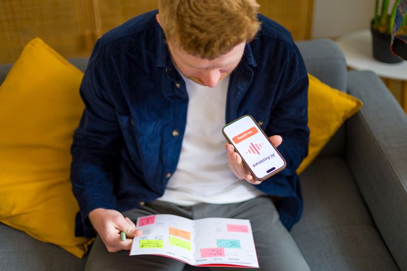 Young man holding a smartphone with an ai assistant app on screen, simultaneously managing tasks in a colorful weekly planner