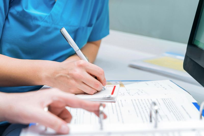 two nurses share patient information by writing it on the patient file, sharing paperwork and reviewing medical chart examination room. medical research or surgery planning in wellness hospita