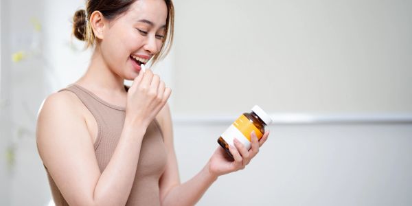 Woman smiling while holding a pill and a supplement bottle.
