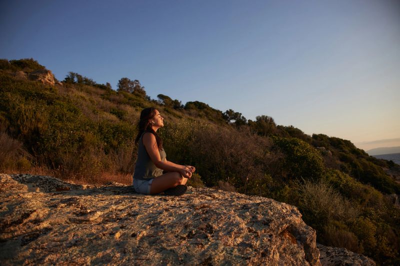 Beautiful woman meditating on the top of the cliff. It is sunrise, charging energy.