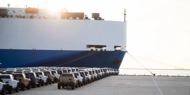 Cargo ship docked with rows of cars waiting.