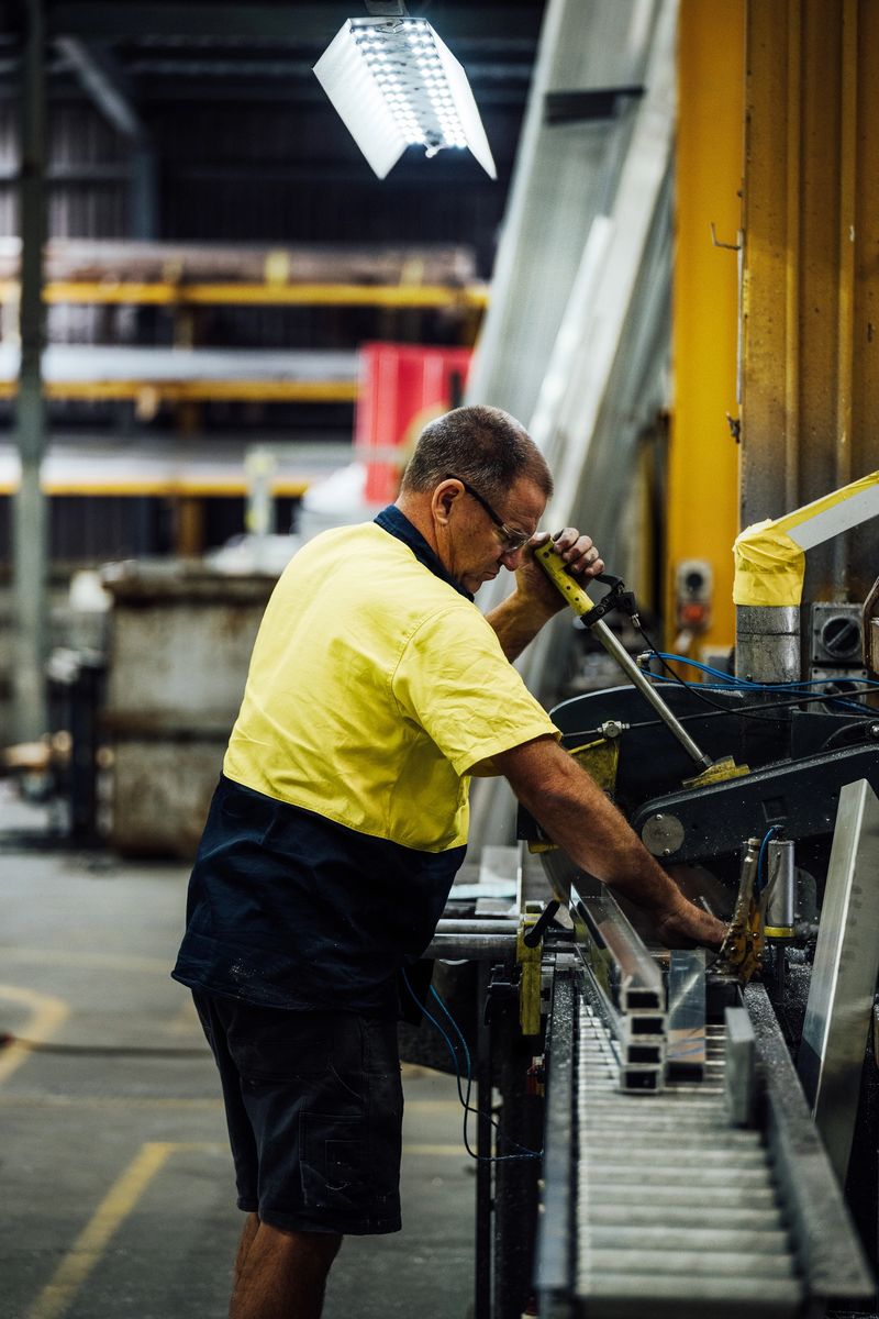 Worker in a factory setting adjusting a machine for processing metal materials in an industrial environment with safety gear