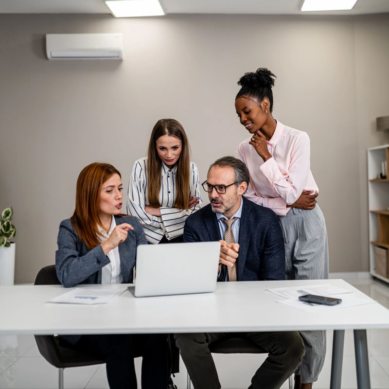 Diverse business professionals analyzing data and discussing strategy on a laptop during an important office meeting