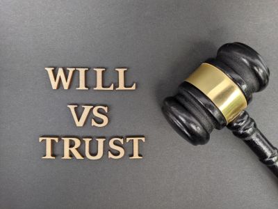 Wooden letters spelling 'WILL VS TRUST' next to a judge's gavel.