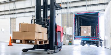 Forklift loading boxes onto a truck inside a warehouse.