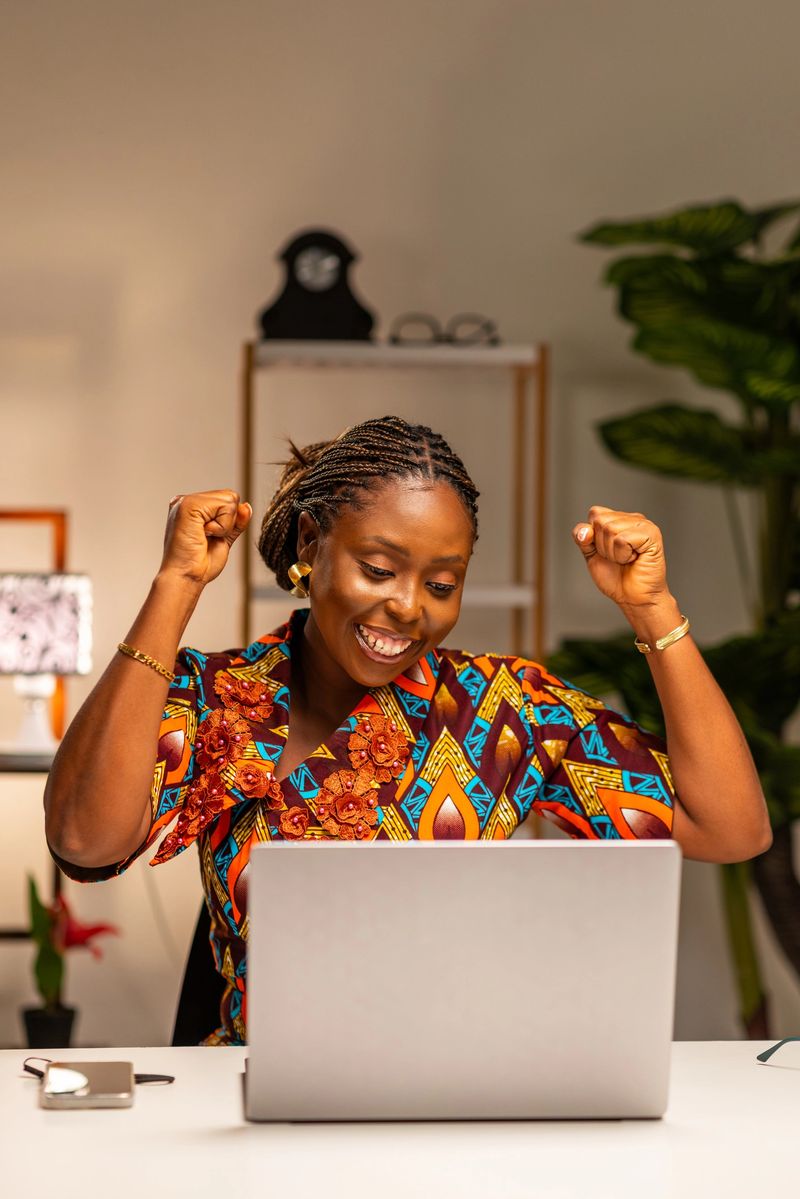 Excited happy African woman with her laptop celebrating an online win, job offer, or personal achievement
