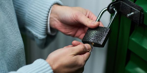 Hands unlocking a black padlock on a green door.
