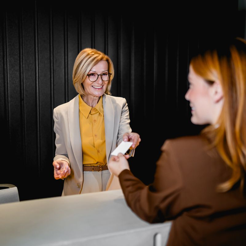 Professional hotel receptionist giving a key card to a guest at the front desk, providing excellent hospitality service