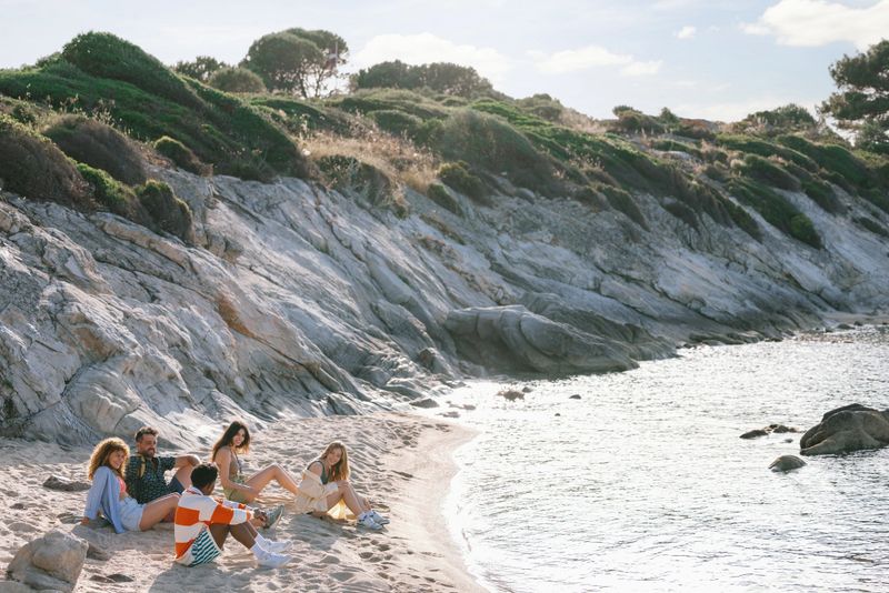 Happy friends relaxing on sand after coastal hike