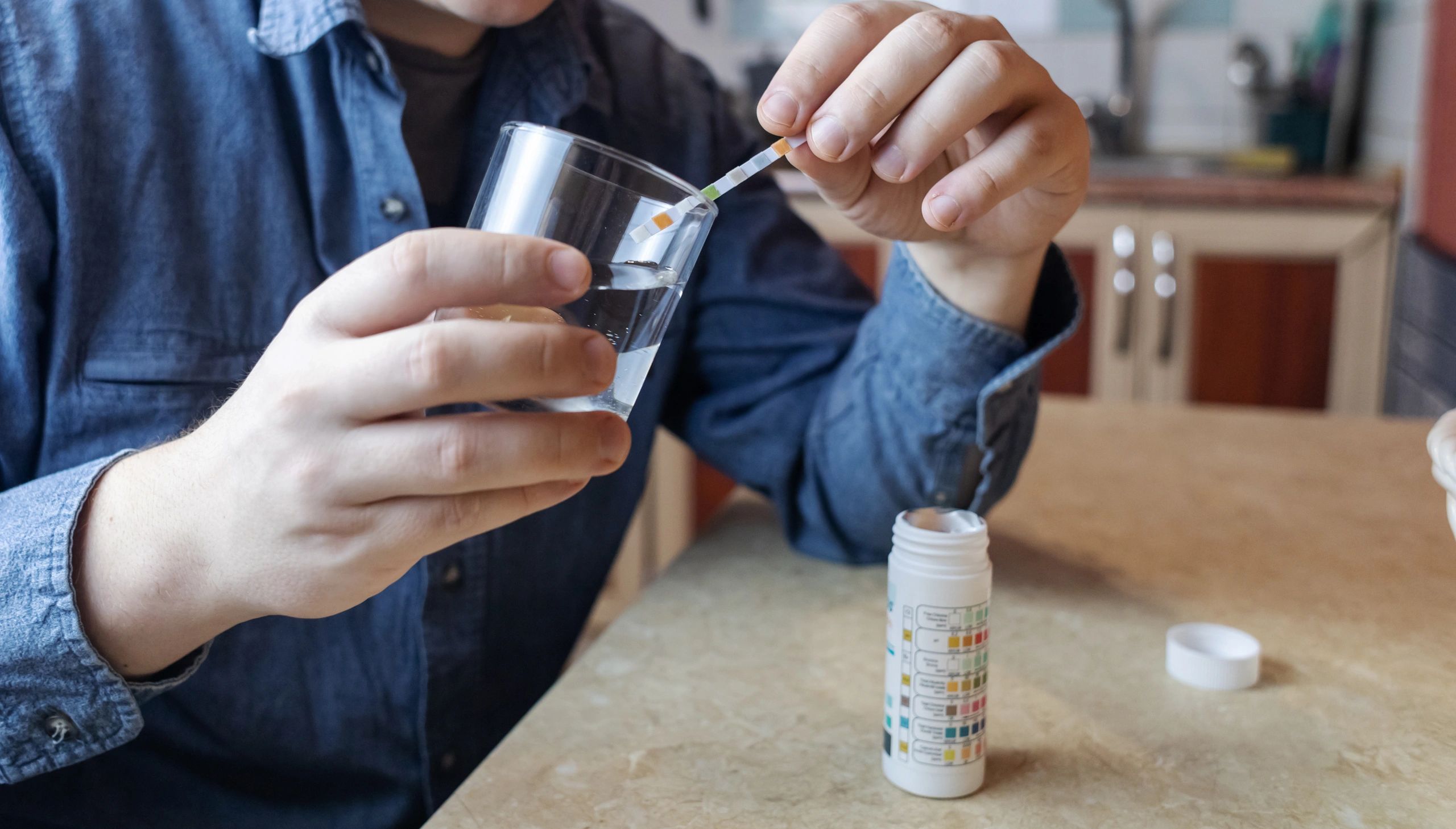 Person testing water quality with a test strip and glass of water.