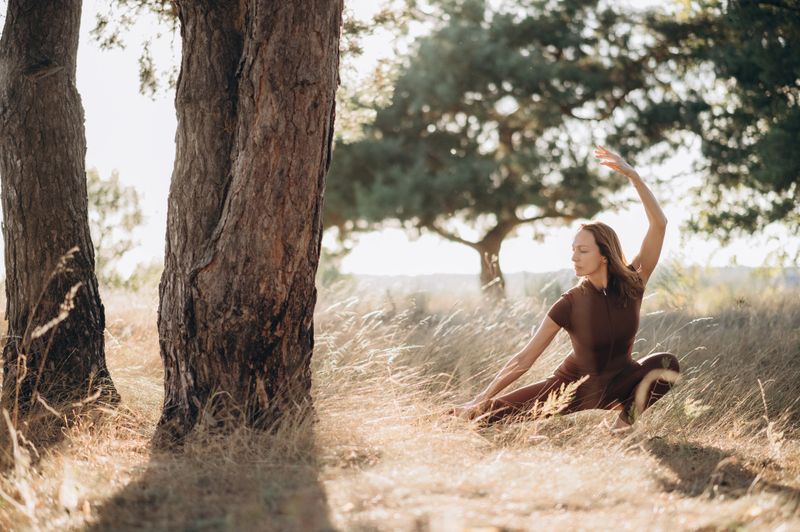 A woman performs a calm yoga pose in nature, enjoying balance, flexibility, and the soft glow of sunlight.