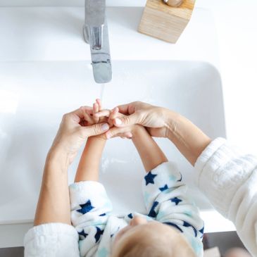Adult washing child's hands under running water.