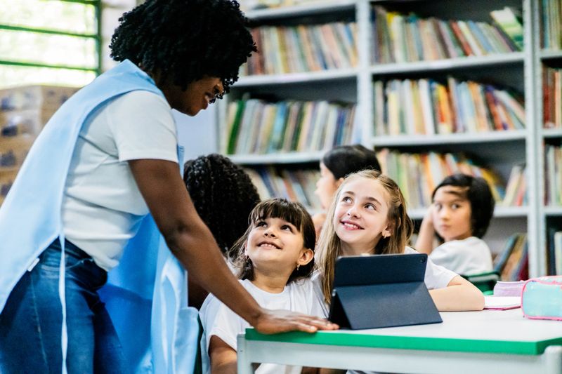 Teacher helps students study using a digital tablet in the school library