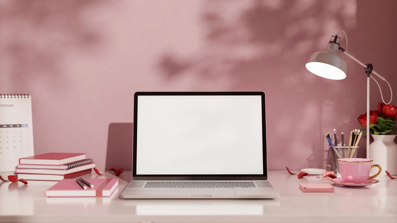 White screen laptop and coffee with books and stationery aside lamp on shiny table in pink wall room. Advertise Mockup, 3D Rendering, 3D illustration.