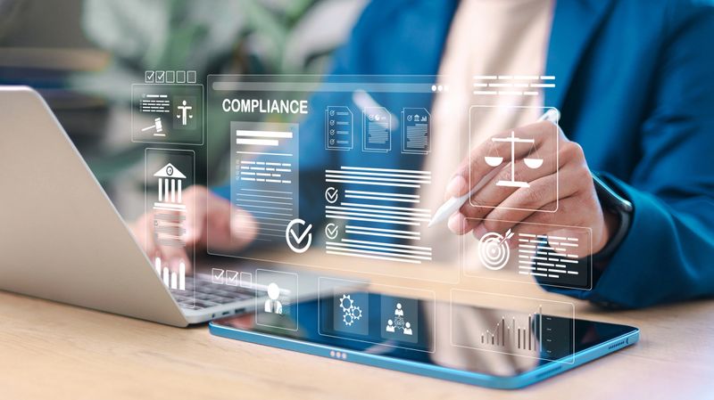 Business professional reviewing digital compliance documents on laptop and tablet. Legal regulation, corporate governance, audit, risk management, and data protection concept.