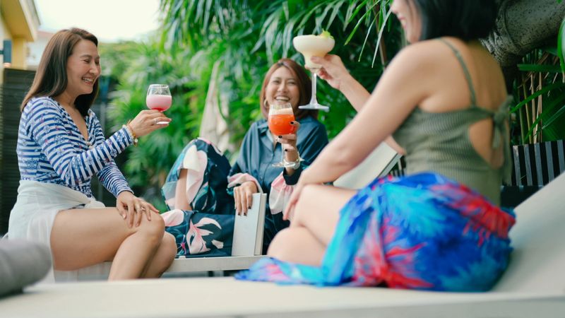 luxury travel concept showing personalized service and relaxation asian women resting on poolside sunbed while staff assists. themes include resort leisure, vacation lifestyle, comfort, and premium hospitality.