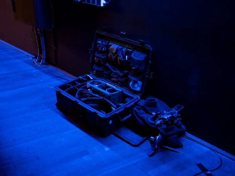 Film production equipment and camera gear on theatre stage floor in blue stage lighting, wide view