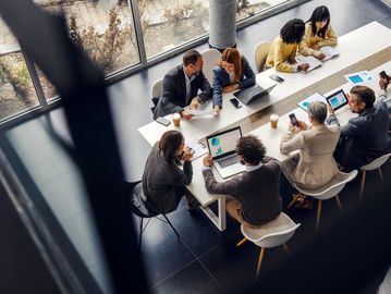 Professionals collaborating around a table with laptops and documents in a modern office.