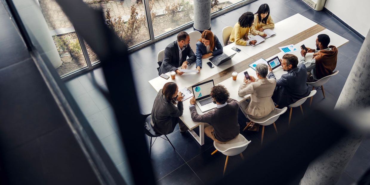 A diverse group collaborates around a modern conference table with laptops and documents.