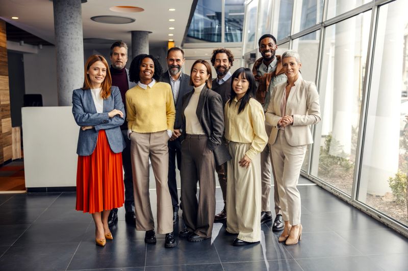 Diverse group of business people smiling, collaborating, and embracing team spirit in a modern office setting, representing success, professionalism, and global partnership