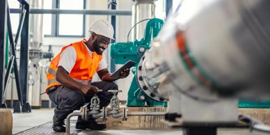 Technician in safety gear inspecting industrial machinery with a tablet.