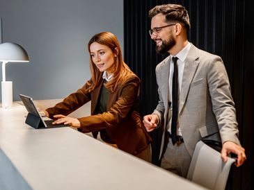 Two business professionals collaborating at a reception desk with a tablet.