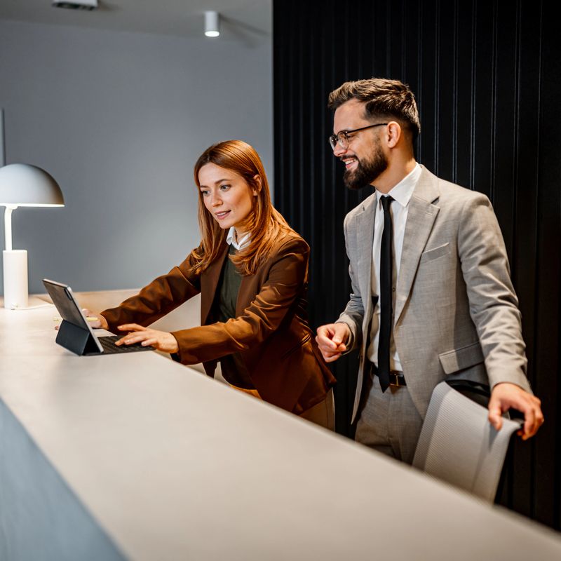 Two business professionals using a digital tablet for work, standing at a reception counter in a modern office environment