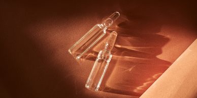 Two glass ampoules on a brown surface with shadows.