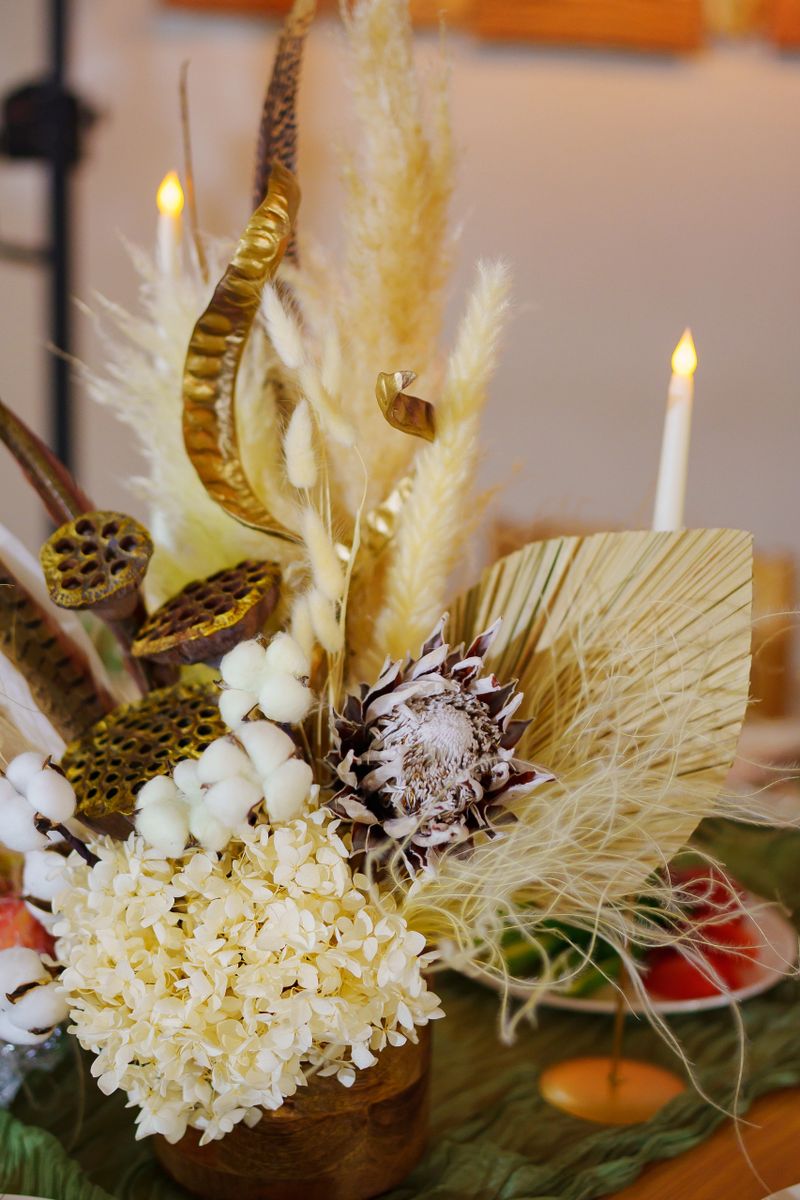 This elegant floral display features dried and fresh flowers in a warm indoor space with soft lighting, creating a calm and inviting atmosphere for guests.