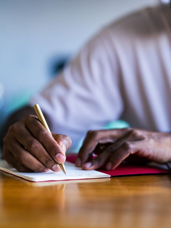 Person writing in a notebook with a pen beside a laptop.