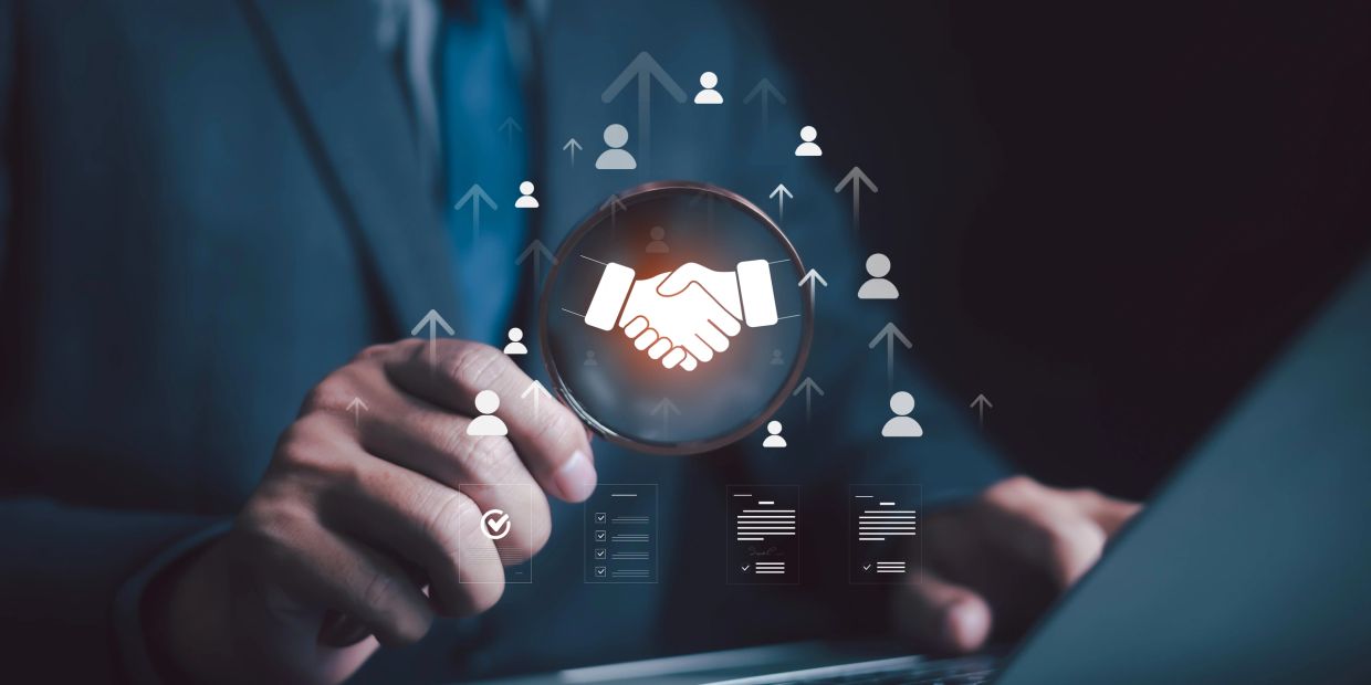 Businessman holding magnifying glass with handshake icon.