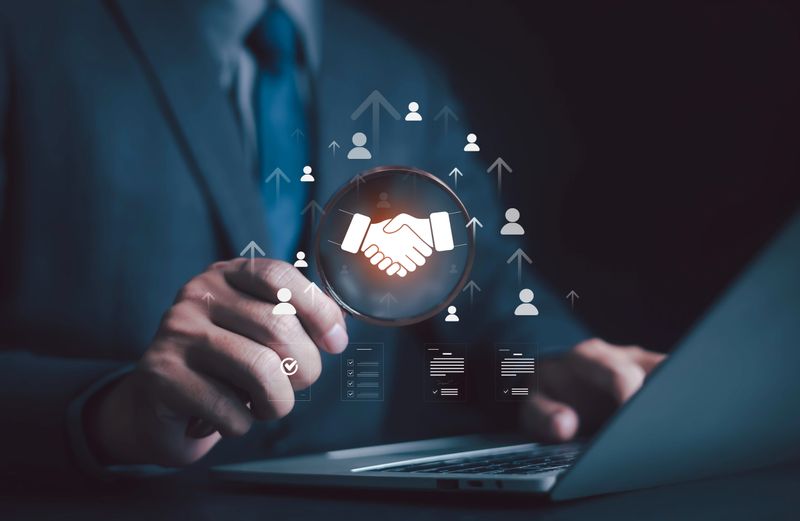 Businessman using laptop with handshake icon, symbolizing business partnership, collaboration, teamwork, networking, contract agreement, digital deal, trust, and professional cooperation.