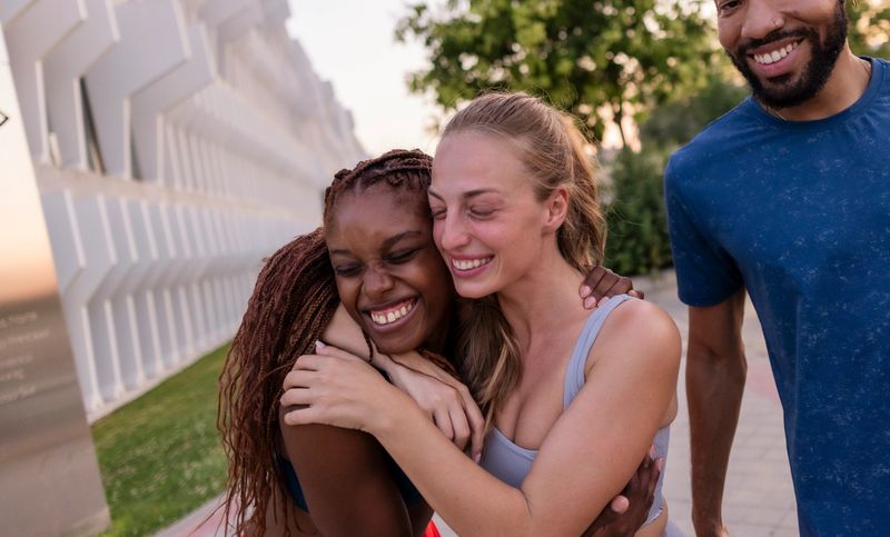 Diverse friends are sharing a happy moment, embracing and smiling widely while enjoying time together outdoors, representing friendship, happiness, connection, and inclusivity