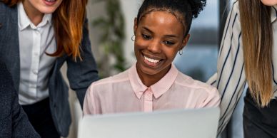 Three women looking at a laptop and smiling.