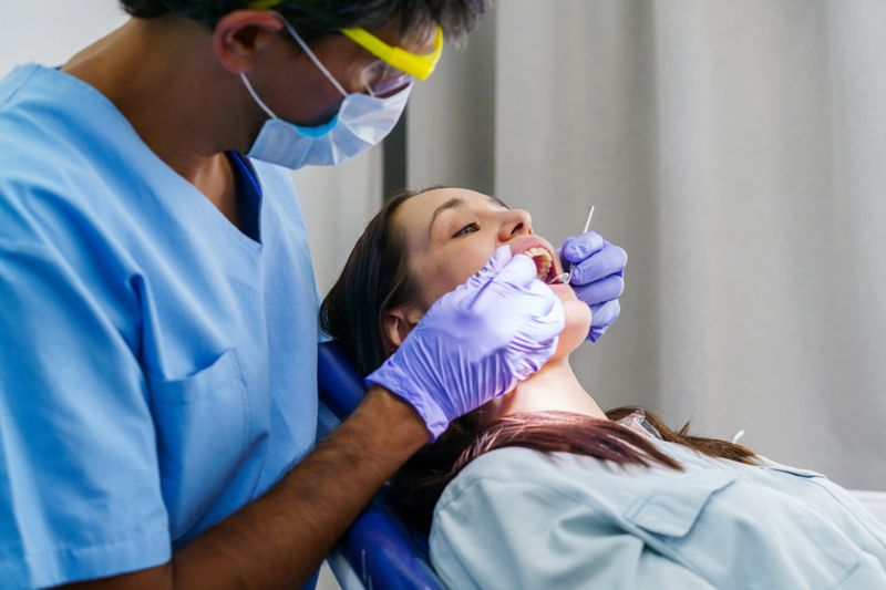 A dentist examines a patient during a dental checkup in a clinical setting. Protective gear and dental tools highlight professionalism, care, and oral health in a healthcare environment.