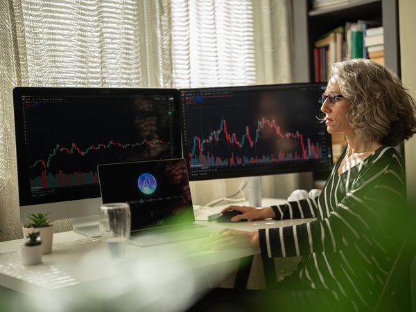 Woman analyzing stock charts on multiple screens in a home office.