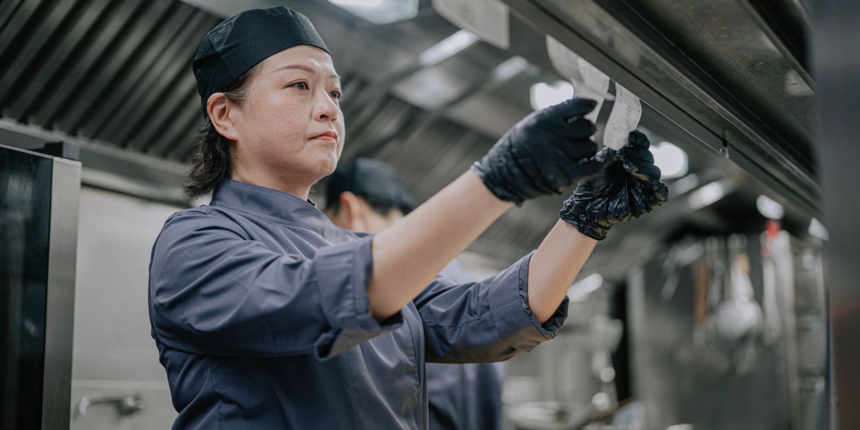 Chef in black uniform checking order tickets in a professional kitchen.