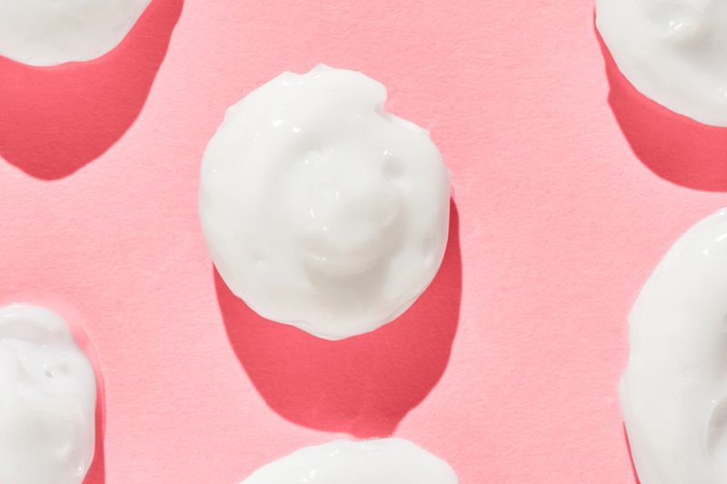 White cream smears on pink background displaying skincare texture and moisturizing concept.