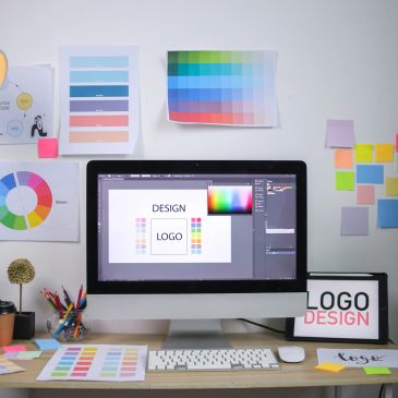 Workspace with computer displaying logo design software and color swatches.
