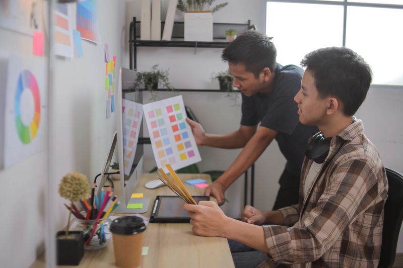 Designers Comparing Color Swatches With Digital Design Mockups for New Brand Identity Project at Office