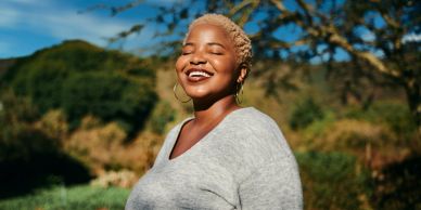 Woman smiling outdoors with eyes closed.