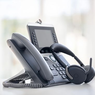 Modern office phone with a headset placed beside it on a desk.