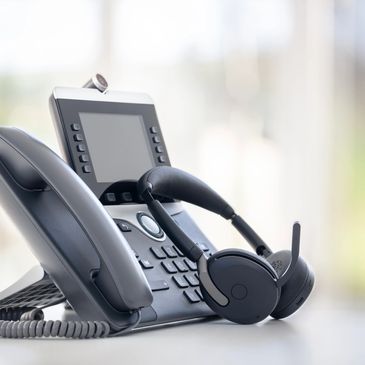 Office desk phone with a wireless headset resting on it.