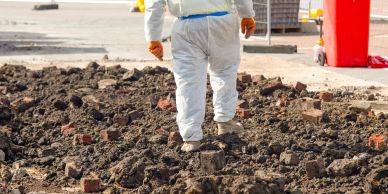 Person in protective suit walks on muddy ground with bricks.