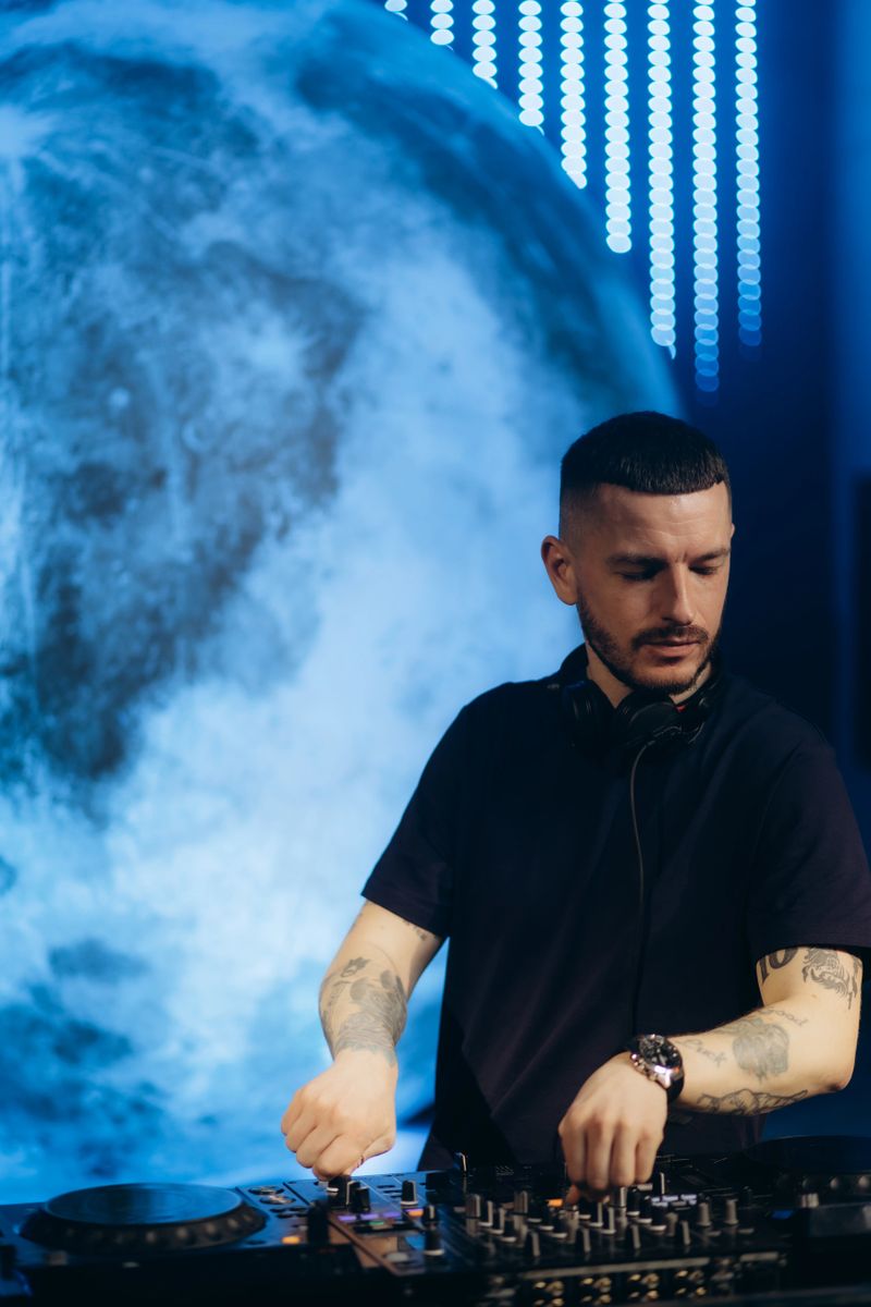 A professional male DJ performing exciting music on a modern mixer under vibrant neon lights.